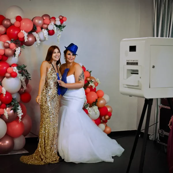 Bruid en vriendin voor een witte Partypimpers photobooth op een trouwfeest